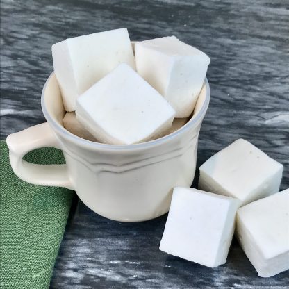 Vanilla marshmallows piled in a ceramic mug setting on a dark marble board with a green napkin