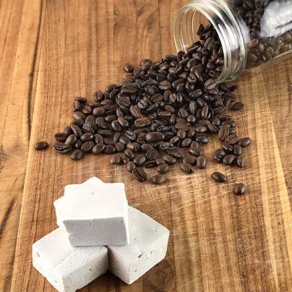 Three coffee marshmallows on a brown board with a jar of spilled coffee beans