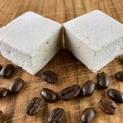Two coffee marshmallows on a brown board with coffee beans sprinkled about.