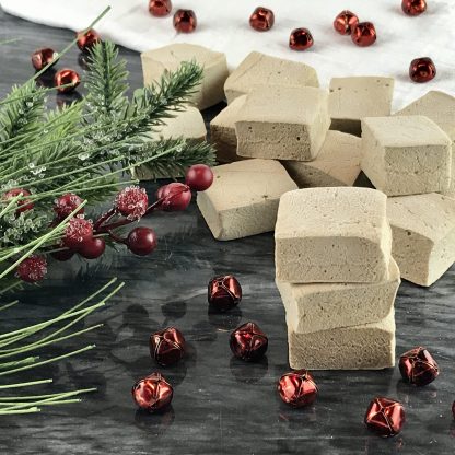 Gingerbread marshmallows on a dark marble board with seasonal greenery and red jingle bells