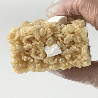 A gloved hand grasping a crisp rice treat with homemade mini marshmallows with a white background
