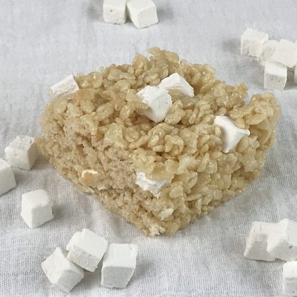A crisp rice treat with homemade mini marshmallows on a white cloth with additional mini mallows sprinkled around
