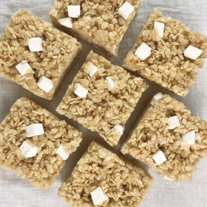 Seven crisp rice treats with homemade mini marshmallows lined up on a white cloth
