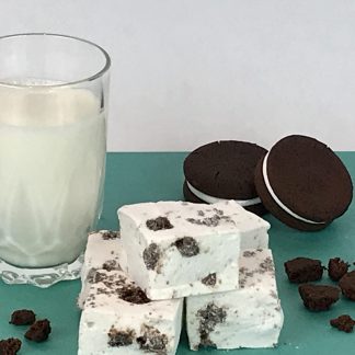 Five cookies and cream marshmallows on green paper with a glass of milk, chocolate sandwich cookies, and cookie crumbles