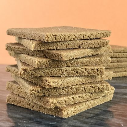A stack of gluten-free graham crackers on a dark marble board. There is another stack of grahams in the background.