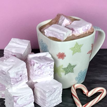 A cup of hot cocoa with peppermint marshmallows melting in it. More peppermint marshmallows and candy canes are near the cup on a dark marble board.