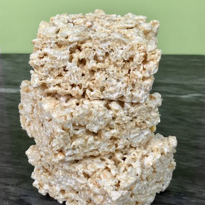 A stack of three Marshmallow Crispies sets on a dark marble board. There is a light green background.