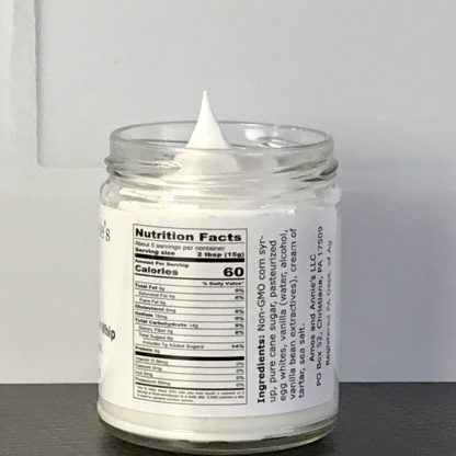 An open jar of vanilla marshmallow whip sits on a dark brown board. The nutrition facts panel is showing. There is a white tile background.