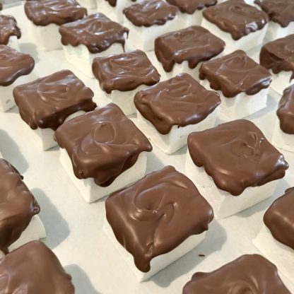 A closeup photo showing vanilla marshmallows topped with Belgian milk chocolate. The marshmallows are on a baking tray.