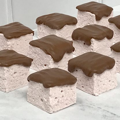 A closeup photo showing strawberry marshmallows topped with Belgian milk chocolate. The marshmallows are on a light gray marble board.