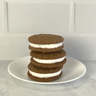Three oatmeal creme pies are stacked on a white plate. The plate is on a white marble board. The background is white subway tile.