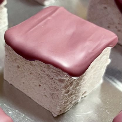 A closeup of a strawberry marshmallow topped with ruby chocolate on a silver sheet pan.