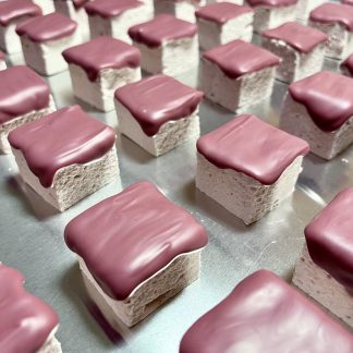 A closeup photo showing strawberry marshmallows topped with Belgian ruby chocolate. The marshmallows are on a silver sheet pan.