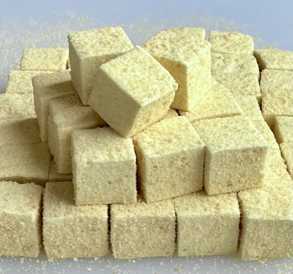 A stack of banana pudding marshmallows on a white board. The marshmallows are yellow and are coated with gluten-free cookie crumbs.