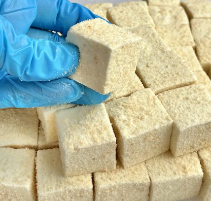 A gloved hand holds a banana pudding marshmallow above a stack of the marshmallows.