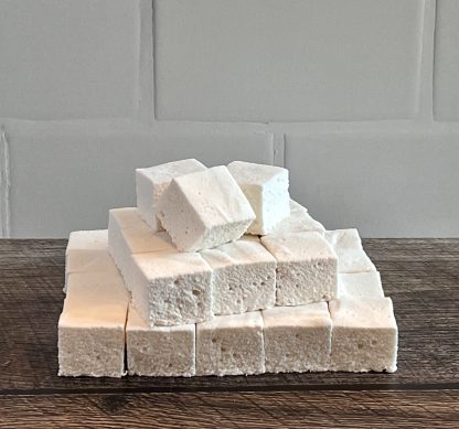 A stack of vanilla marshmallows on a brown board. The background is white subway tile.