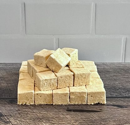 A stack of maple marshmallows on a brown board. The background is white subway tile.