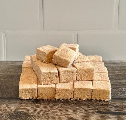 A stack of apple cider donut marshmallows on a brown board. The background is white subway tile.