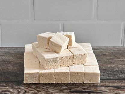 A stack of peanut butter marshmallows on a brown board. The background is white subway tile.