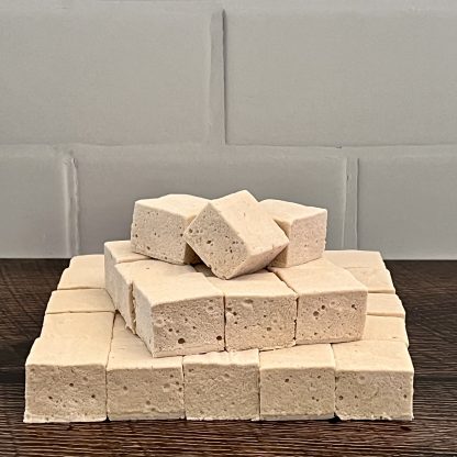 A stack of coffee marshmallows on a brown board. The background is white subway tile.