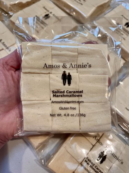 A hand holds a package of salted caramel marshmallows above other packages on a table.