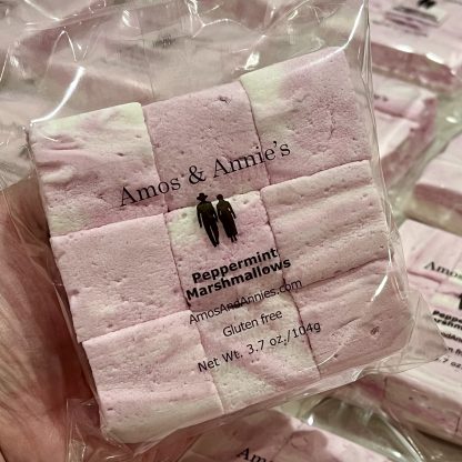 A hand holds a package of peppermint marshmallows above other packages on a table.