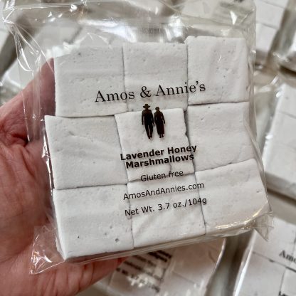 A hand holds a package of lavender honey marshmallows above other packages on a table.