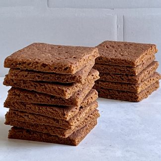 A stack of gluten-free graham crackers on a light marble board. There is another stack of grahams in the background. The background wall is white subway tile.